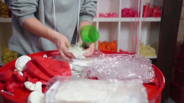 Woman aerodesigner fills transparent balloon with white feathers through funnel — Stock Video