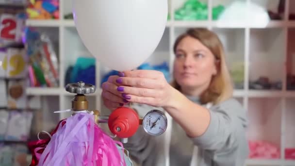 Een vrouw blaast helium op uit een witte ballon. — Stockvideo