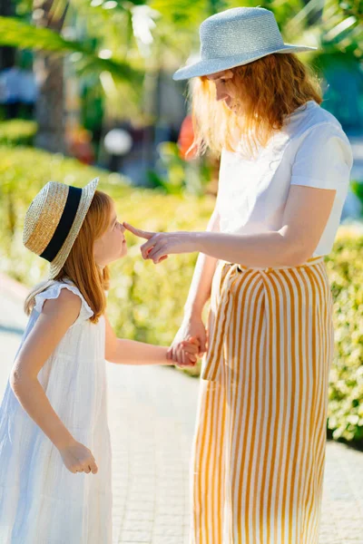 Anne ve kızı otelin tropikal parkında şapka takıyor.