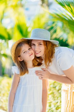 Anne ve kızı otelin tropikal parkında şapka takıyor.