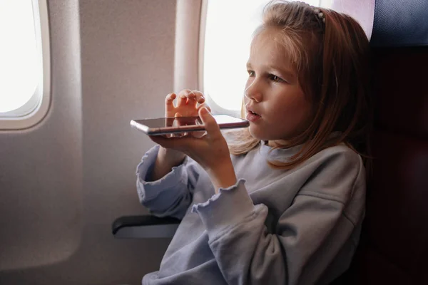 A little girl is talks hands-free calls on the phone in an airplane seat — Stockfoto