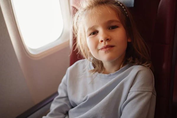 Una niña divertida se sienta en un asiento de avión junto a la ventana. — Foto de Stock