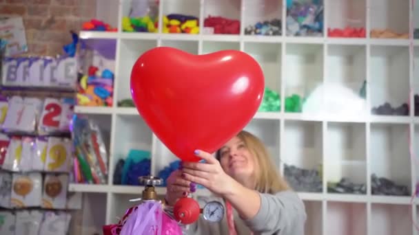 En kvinna blåser upp helium från en ballong i form av ett hjärta. — Stockvideo
