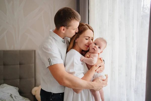 a happy family with a newborn baby by the window. mom, dad and baby.