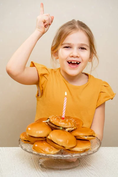 A funny kid little girl makes a wish and blows out a candle on a hamburger cake. Royalty Free Stock Photos