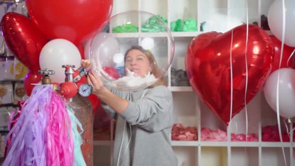 Femme gonfle à l'hélium un ballon transparent avec des plumes blanches à l'intérieur. — Video