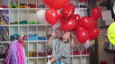 Kadın, beyaz, kırmızı, folyo balonlardan kalp ve top şeklinde kompozisyon yapar.. 