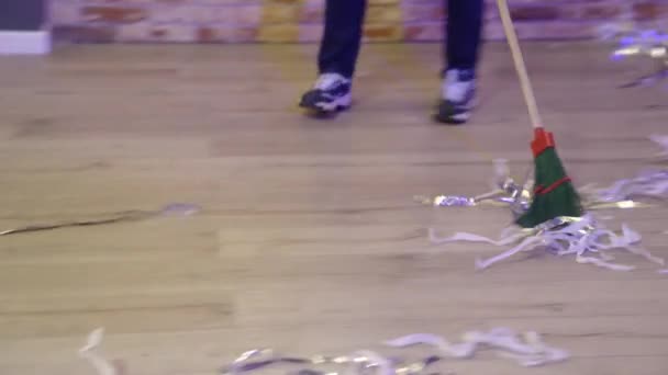 En man sopar konfetti och sopor med en kvast efter en fest. — Stockvideo