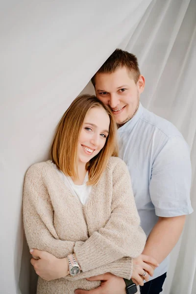 Um casal feliz e amoroso abraços contra o fundo de uma cortina branca. — Fotografia de Stock