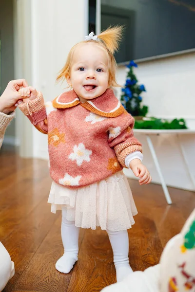 Χαριτωμένο κοριτσάκι σε ένα ροζ πουλόβερ με λουλούδια κρατά το χέρι μαμάδες. πρώτα βήματα — Φωτογραφία Αρχείου