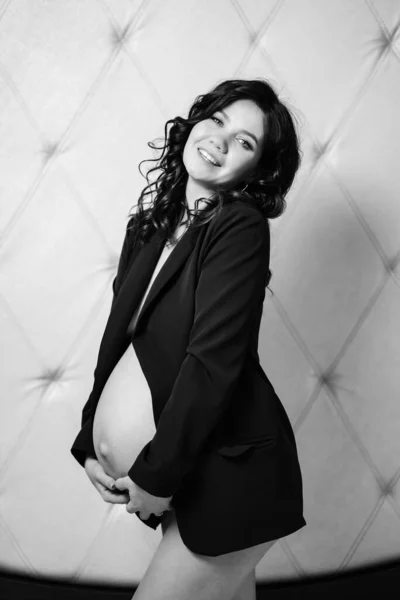 En glad gravid kvinna i svart jacka med bara bröst och en mage — Stockfoto