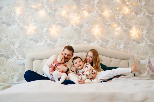 Una familia feliz con dos niños se encuentra en una acogedora cama en el dormitorio de la casa. — Foto de Stock