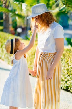 Anne ve kızı otelin tropikal parkında şapka takıyor.