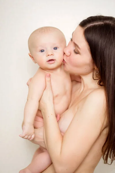 Egy gyönyörű és gyengéd anya megcsókolja a babát a falnak. — Stock Fotó