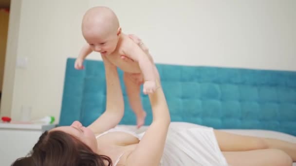 Una madre juega con el bebé en la cama. salud materna e infantil. — Vídeos de Stock