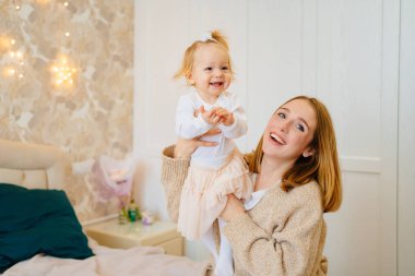 Sevimli anne ve bebek kız uzanıp, yatakta oynaşıp, sarılıyorlar. Çocuklarla oyunlar. 