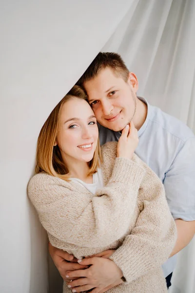 Um casal feliz e amoroso abraços contra o fundo de uma cortina branca. — Fotografia de Stock