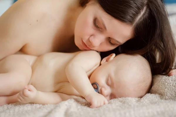 Egy gyönyörű meztelen baba alszik az anyja mellett az ágyban. az anyaság boldogsága. — Stock Fotó