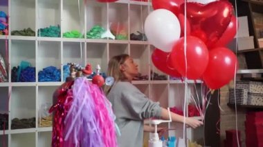 Kadın, beyaz, kırmızı, folyo balonlardan kalp ve top şeklinde kompozisyon yapar.. 