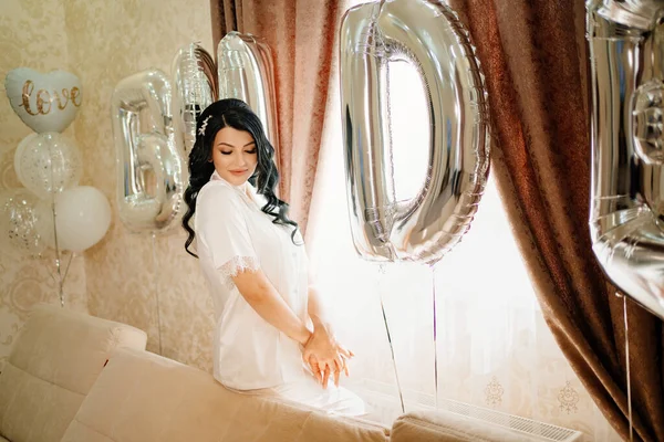 Novia en abrigo blanco en una habitación de su casa por sofá con globos. — Foto de Stock