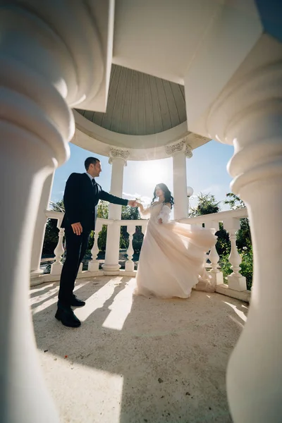 Bruid en bruidegom in trouwkleding dansen in tuinhuisjes of rotonde in het park. — Stockfoto