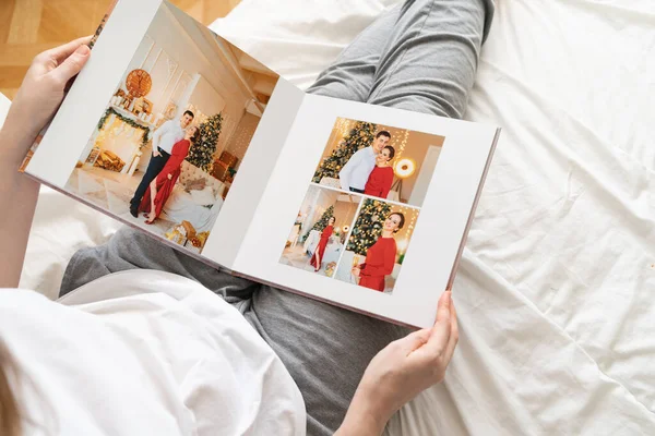 Üst görüşlü kadın yatakta otururken fotobook 'u elinde tutuyor. Aile fotoğrafı çekimi. 