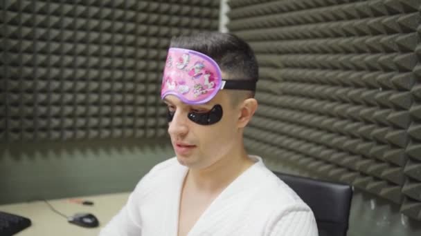 Un présentateur de radio drôle dans un masque de sommeil, peignoir et correctifs cosmétiques — Video