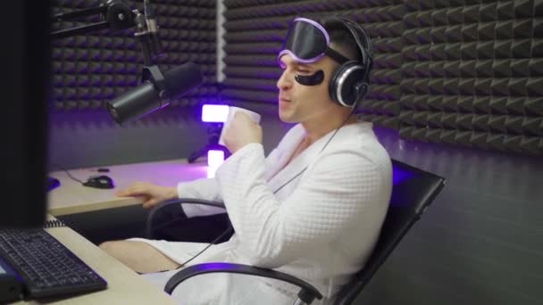 Radio presenter in sleep mask and cosmetic patches drinking coffee on air — Stock Video