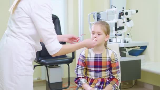 Ophtalmologiste ramasse des lunettes pour une petite fille à un rendez-vous dans une clinique — Video