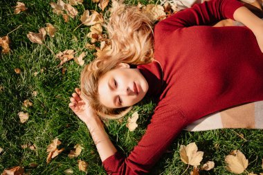 Çekici sarışın bir kadın sonbahar yapraklarıyla yeşil bir çimenlikte yatıyor.. 