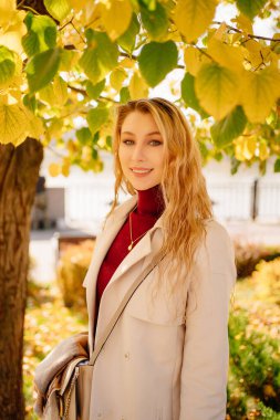 Paltolu ve kot pantolonlu güzel bir sarışın sonbahar parkında yürüyor. 