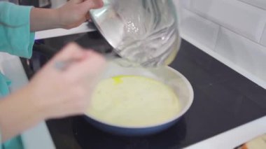 Bir kadın omlet hazırlar ve bir tavaya süt ve yumurta karışımı döker.
