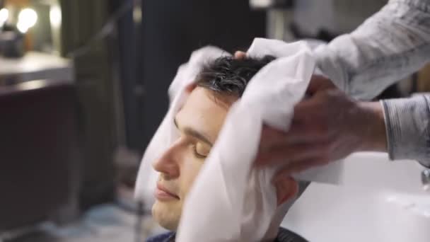 美容師は髪を洗った後使い捨てタオルでブルネットの男の髪を拭く — ストック動画
