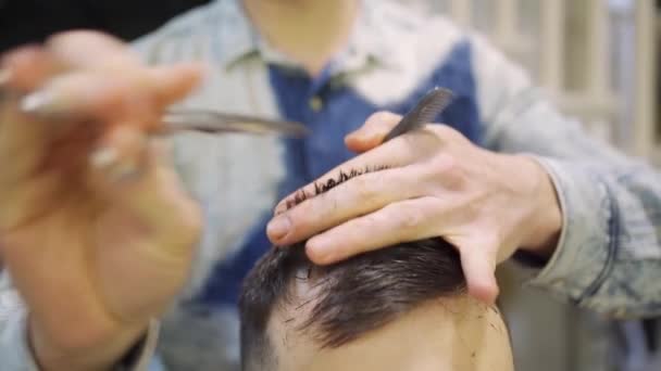 Fecha. cabeleireiro faz um corte de cabelo para um homem com uma tesoura em uma barbearia — Vídeo de Stock