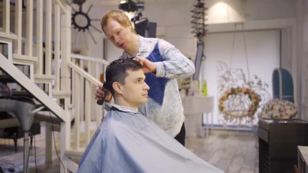 O cabeleireiro faz um corte de cabelo para um homem com um cortador de cabelo em uma barbearia — Vídeo de Stock