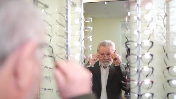 An elderly man tries on and chooses glasses in the optics salon. — Stock Video