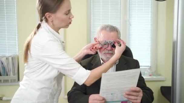 Oftalmólogo hace la selección de lentes, diagnostica la visión de un anciano. — Vídeo de stock