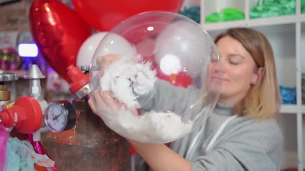 Kobieta napełnia helem przezroczysty balon z białymi piórami wewnątrz. — Wideo stockowe