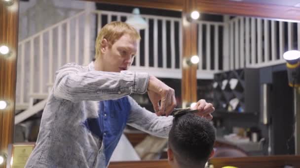 Frisörsalong. frisör gör en frisyr för en brunett man med en sax. — Stockvideo