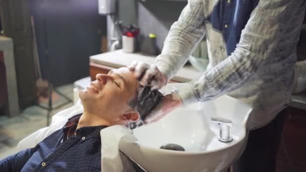 ブルネットの男が理容室で美容師と髪を洗う. — ストック動画