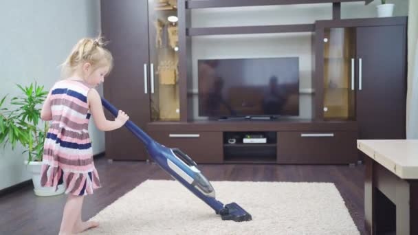 Nettes kleines Mädchen putzt selbstständig Teppich im Zimmer mit Staubsauger — Stockvideo