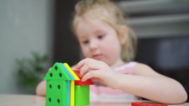Sevimli küçük bir kız renkli ahşap bir inşaat setinden evler inşa ediyor.. — Stok video