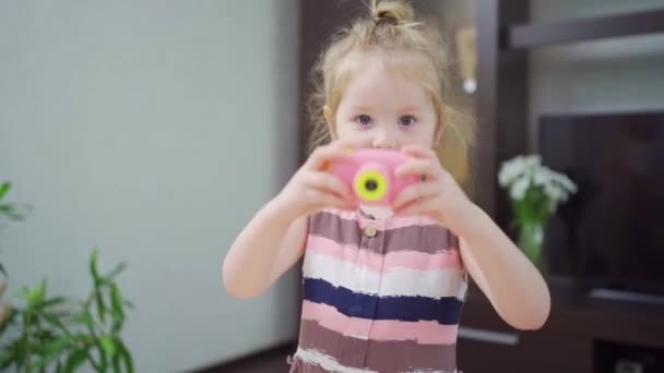 Komik küçük bir kız küçük pembe bir oyuncak kamerayla fotoğraf çekiyor.. — Stok video