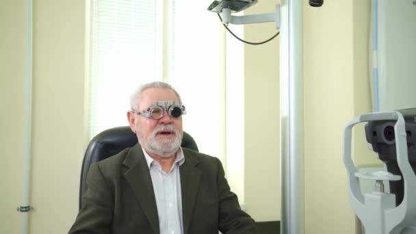 Ögonläkare diagnostiserar äldre mans syn och gör urval av linser. — Stockvideo