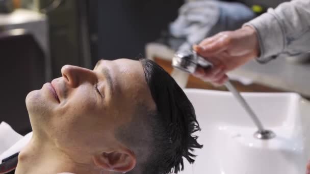 Una peluquera lava el pelo de un hombre moreno en una peluquería. — Vídeo de stock