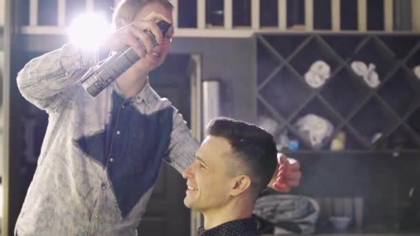 O cabeleireiro styling um homem morena e pulverização hairspray em uma barbearia — Vídeo de Stock