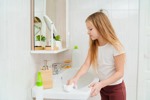 Милая маленькая девочка моет раковину в ванной со специальным чистящим средством. — стоковое фото