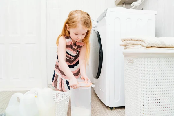 Egy aranyos kislány kinyitja a mosóport a mosógépnek. Stock Kép