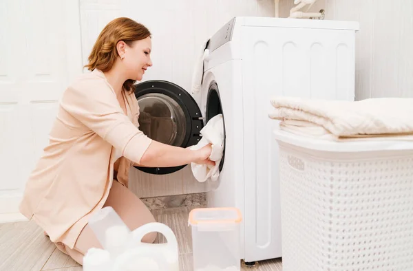 En kvinde sætter vasketøj i vaskemaskinen. Stock-billede