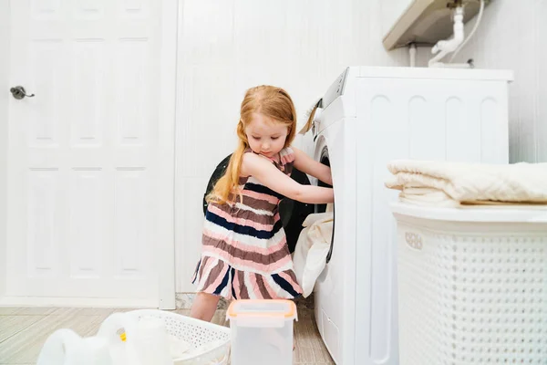 En sød lille pige sætter vasketøj i vaskemaskinen. Stock-billede